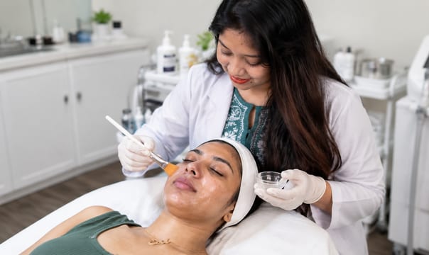 Clinician brushing a chemical peel solution onto a reclining patient's face