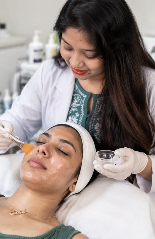 Clinician brushing a chemical peel solution onto a reclining patient's face